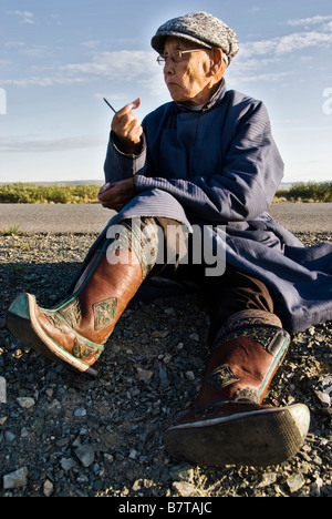 Old Mongolian man, dressed in a traditional way, eating during a rest in a long bus ride, Mongolia. Stock Photo