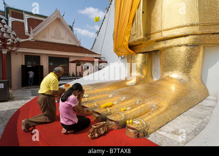 Buddhists praying at feet of 32m golden standing buddha Wat Intharavihan temple in Dusit district of Bangkok in Thailand Stock Photo
