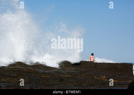 Wave breaking on rocks person holding on Stock Photo