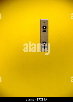 Vintage up and down elevator buttons on a stainless steel panel in the middle of a painted yellow wall. Stock Photo