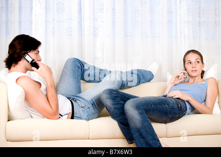 Young man and woman lying on sofa both using mobile phones side view Stock Photo