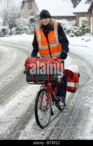Woman postal worker cycling in snowy roads in Aberdeenshire, Scotland, UK, during winter Stock Photo