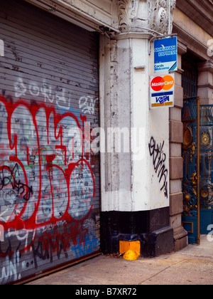 Major credit card logos on a sign affixed to a concrete column beside a steel security door covered in graffiti. Stock Photo