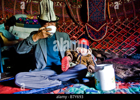 Old Kyrgyz man and grandson drinking horse milk inside his yurt Kyrgyzstan Stock Photo