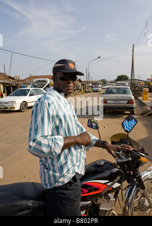 A Nigerian man poses in the sun on his motorcycle in the street of Poka, Epe Stock Photo