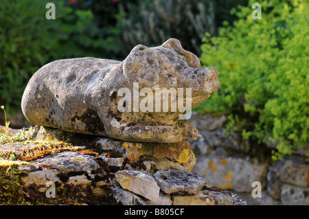 Stone pig sitting on an old stone wall covered in lichen and moss Stock Photo