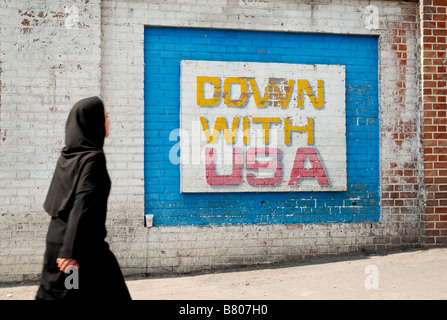 tehran black cloak wearing muslim woman walking past anti american mural outside old american embassy in teheran iran Stock Photo