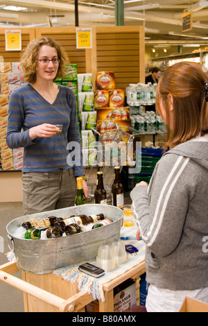 Young woman offers free samples of beer to another young woman in grocery store