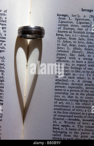 Close up of a heart shaped shadow created from light falling on a wedding ring located next to words about love in a dictionary Stock Photo