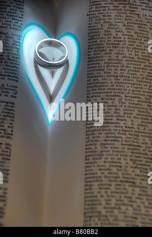 Close up of a heart shaped shadow created from light falling on a wedding ring located next to words about love in a dictionary Stock Photo