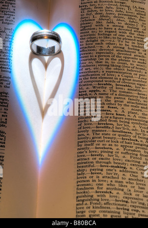 Close up of a heart shaped shadow created from light falling on a wedding ring located next to words about love in a dictionary Stock Photo
