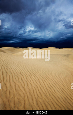 Ripples in the sand on top of Tawny Dunes rising nearly 100 feet from Mesquite Flat with dark ominous storm clouds overhead Stock Photo