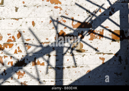 Shadow of security spikes on top of a wall, on a whitewashed brick wall with paint peeling/flaking off. Stock Photo