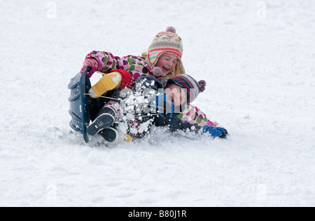 Young children falling off sledge in deep snow Cleeve Hill Cotswolds UK Stock Photo