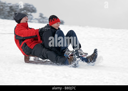 Man woman sledging in deep snow on slopes of Cleeve Hill Cotswolds UK Stock Photo
