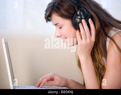 Young woman lying with eyes closed wearing headphones using laptop Stock Photo