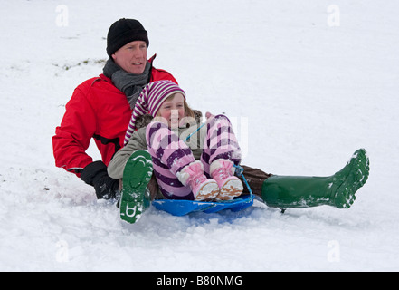 Father and children sledging in deep snow Cleeve Hill Cotswolds UK Stock Photo