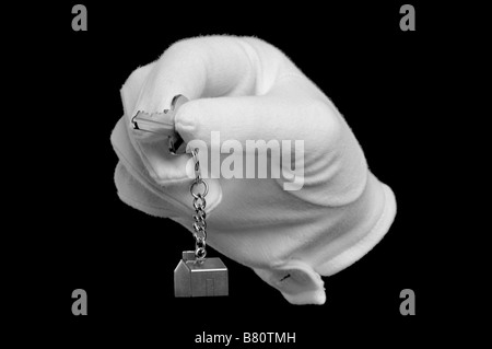 A hand in a white glove holding the key to a new house isolated on black Stock Photo