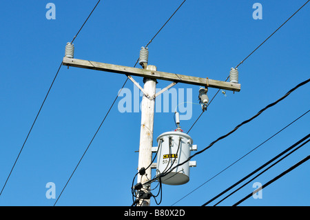 Single electrical transformer on wood telephone pole showing electric cables and insulators against clear blue sky Stock Photo