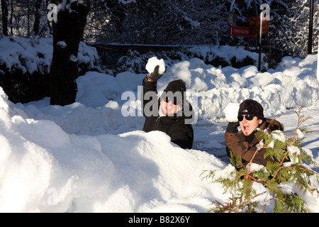 Two young men playing in the snow, hidden to throw large snow balls Stock Photo