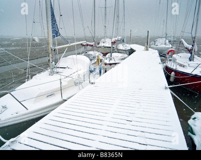 Snow covered boats along side pontoon at low tide Stock Photo