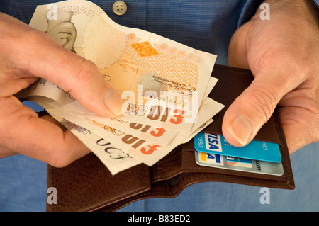 Man holding and taking out English bank notes money from a wallet with bank credit cards close up Stock Photo