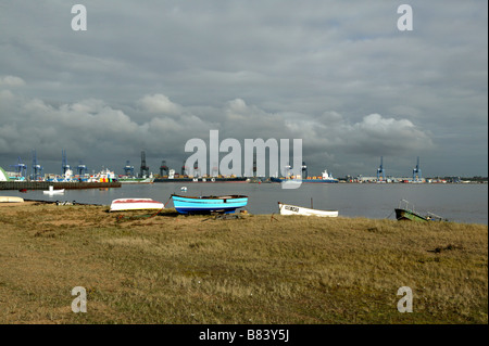 A View across Harwich harbour towards the large commercial cranes of the commercial port with small boats pulled onto the shore Stock Photo