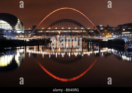 Gateshead Newcastle Millenium Bridge spans the river Tyne bathed in coloured spotlights with Tyne Bridge silhouetted behind. Stock Photo