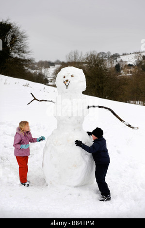 A YOUNG GIRL AND BOY BUILDING A SNOWMAN IN THE COTSWOLD HILLS GLOUCESTERSHIRE UK Stock Photo