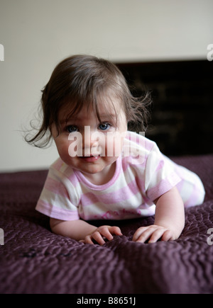 A six month old baby girl crawling on a bed Stock Photo