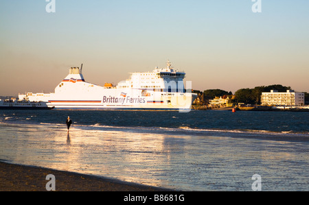 The Brittany Ferries cargo ship Cotentin leaving Poole harbour, Dorset. UK. Reflection in wet sand. Evening sun. Winter. Stock Photo