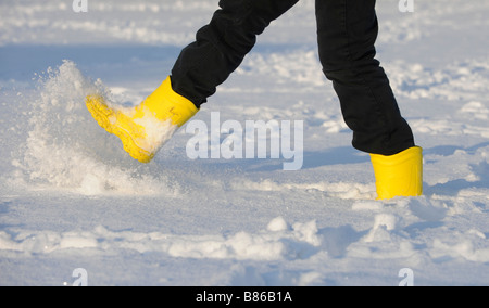 A young woman wearing yellow crocs boots splashing around in the snow. Picture by Jim Holden. Stock Photo