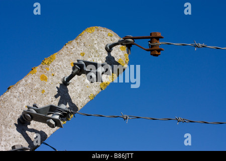 Tip of pre cast concrete security fence post with rusty barbed wire tensioner and 2 strips of barbed wire against blue sky Stock Photo