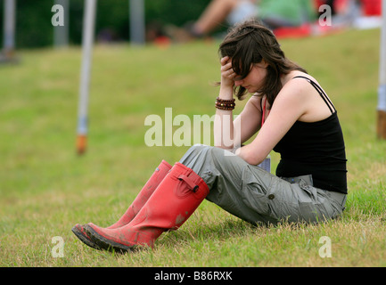 A girl in wellies holds her head after a heavy night out at the Glastonbury festival in Pilton, Somerset in the UK. Stock Photo