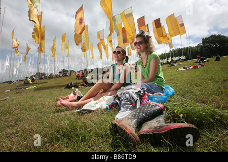 A pair of girls enjoy the sunshine sat among flags at the Glastonbury Festival in Pilton, Somerset in the UK. Stock Photo