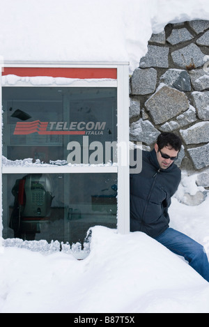 young man getting out of a snow buried telephone box in Italy Stock Photo