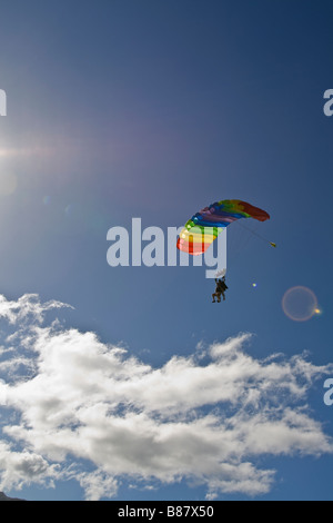 Skydiver couple under canopy are flying over some clouds in the sky and getting ready to land on the beach from Oahu, Hawaii. Stock Photo