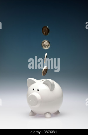 Concept finance saving - Pound coins sterling falling into a piggy bank - studio Stock Photo