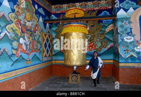 A young Bhutanese man in traditional dress stands by a giant prayer wheel. Stock Photo