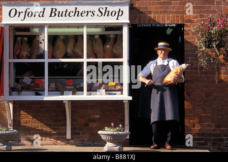 A traditional butcher proudly displays a cut of meat in the doorway of his local butchers shop. Orford Woodbridge Suffolk UK Stock Photo