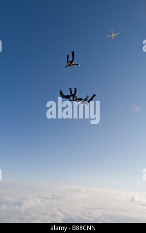 Skydiver team flying a formation in the sky over clouds and holding grips. Camera flyer is taking video images above the divers. Stock Photo