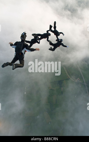 Skydiver team flying a formation in the sky over clouds and holding grips. Camera flyer is taking video images above the divers. Stock Photo