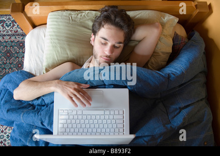 A young man using his laptop computer while still lying in bed. Stock Photo