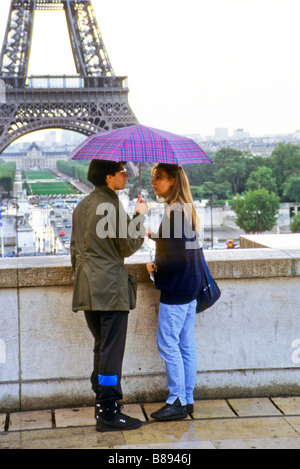 Young couple talk beneath umbrella by wall of the Trocadero with Eiffel Tower in distance paris france Stock Photo