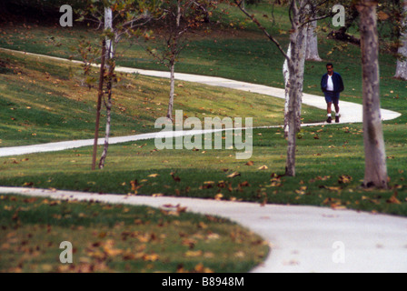 Man walks down curved sidewalk through park Stock Photo