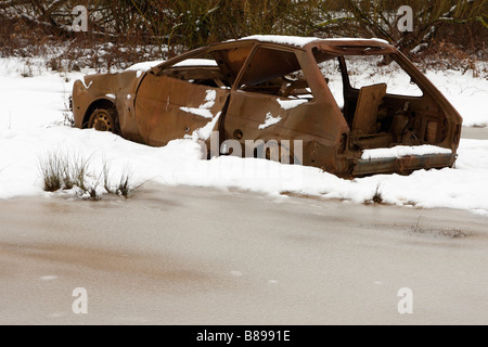 'Burnt out' abandoned car in snow covered field, England, UK, Winter Stock Photo