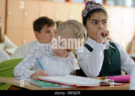 Two schoolgirls in a multicultural classroom. On the left a Christian Ukrainian girl, on the right a Muslim Tatar girl. Stock Photo