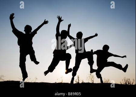 Silhouette profile of young Indian boys jumping against a setting sun background. India Stock Photo