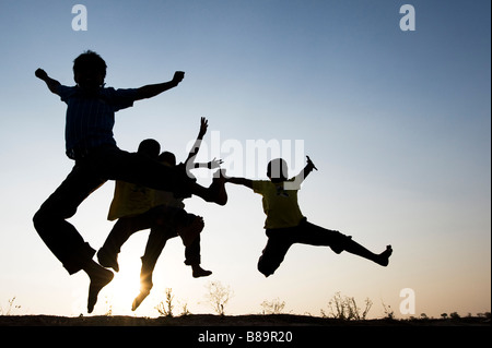Silhouette profile of young Indian boys jumping against a setting sun background. India Stock Photo