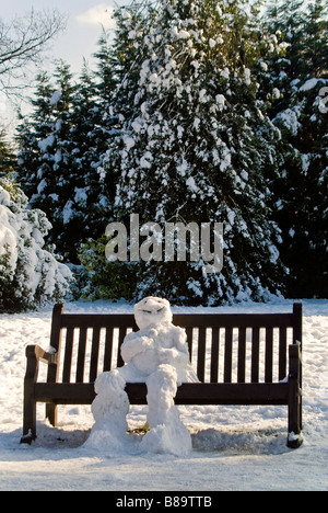 Vertical close up portrait of a traditional snowman sitting on a park bench slowly thawing in the sunshine Stock Photo